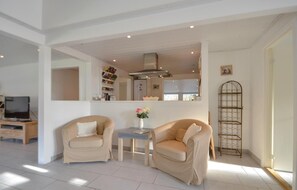 A living room with two beige armchairs, a small table with a vase of flowers, and a metal shelf unit. - Beautiful home in Ebeltoft with kitchen (Ebeltoft)