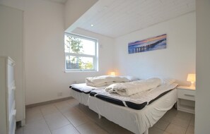 Ein Schlafzimmer mit einem Bett, einem Fenster, einem Gemälde und einem Nachttisch mit einer Lampe.