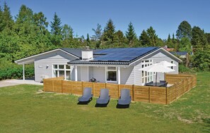 Et etplanshus med solpaneler på taget, en overdækket terrasse med udendørs siddepladser og en indhegnet have.