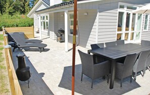 Eine Terrasse im Freien mit Tisch, Stühlen, einem Grill und Liegestühlen.