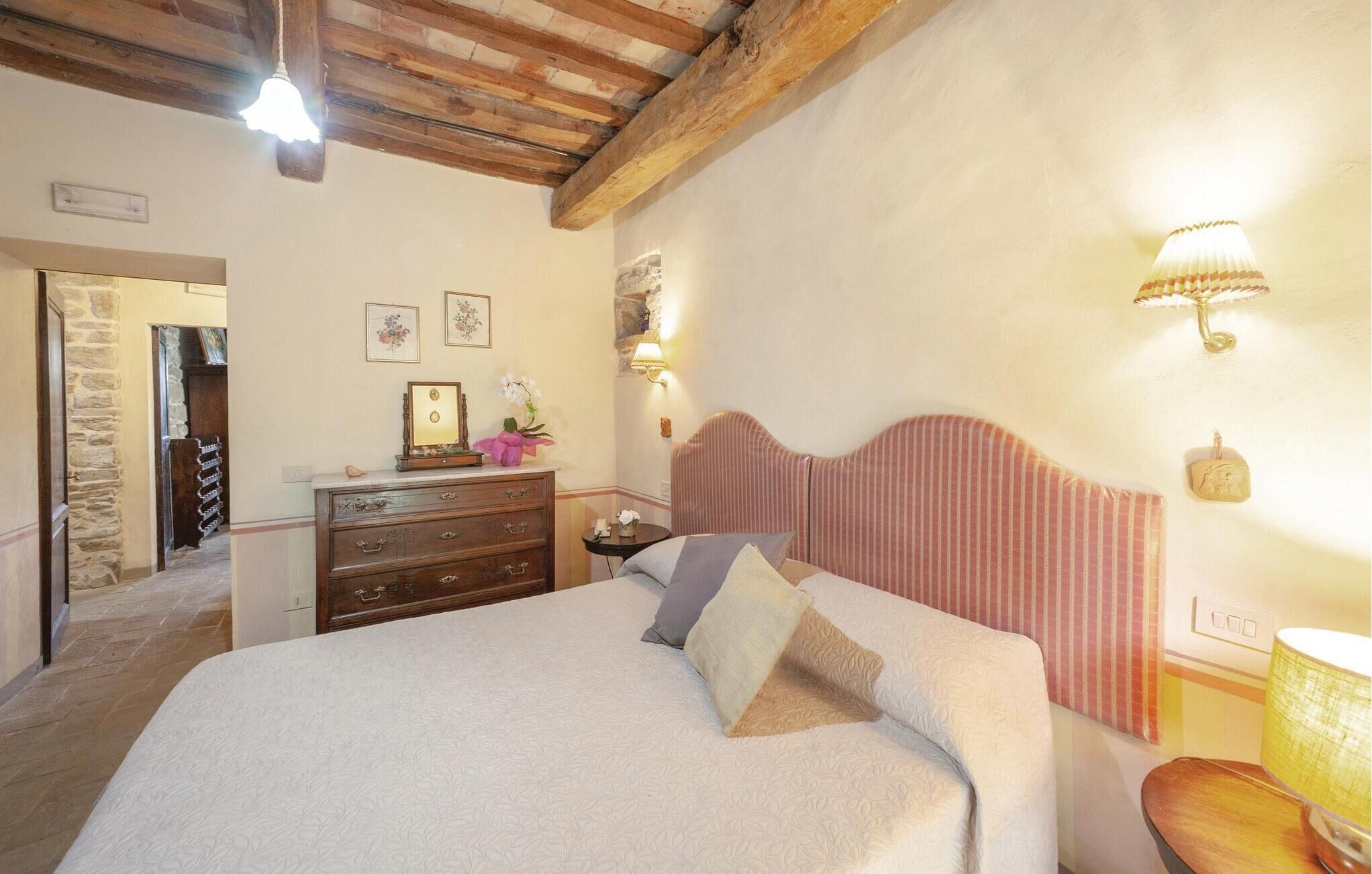 Een slaapkamer met een houten hoofdbord, een dressoir, een nachtkastje met een lamp en een bed met kussens.