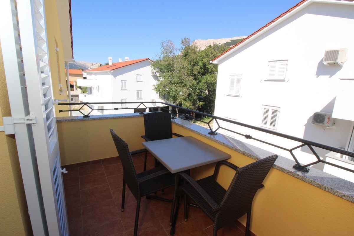 Ein Balkon mit Tisch und Stühlen, einem Geländer und Blick auf Gebäude und Bäume.