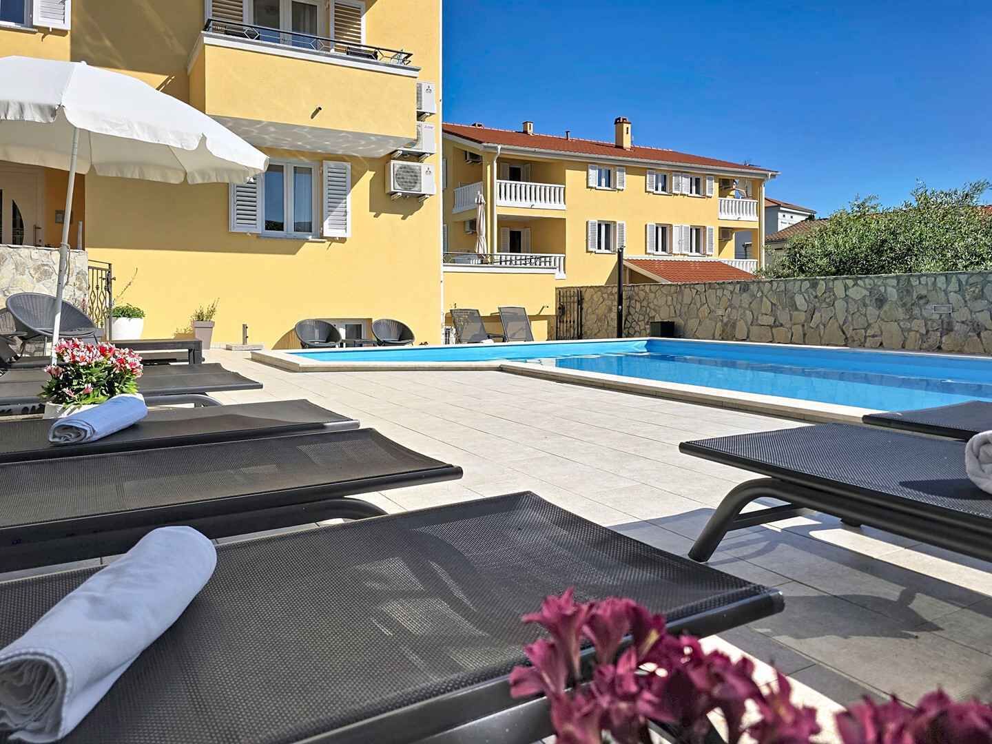 Un área junto a la piscina con sillas de descanso, una sombrilla blanca y una pared de piedra.