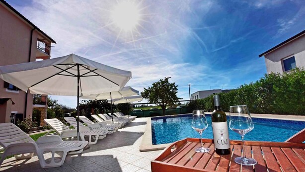 A poolside area with lounge chairs, umbrellas, and a table with a bottle of wine and a glass. - Studio with pool and air conditioning (Novigrad)