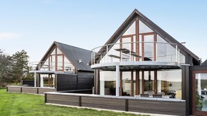 Ein modernes, zweistöckiges Haus mit einem großen Balkon und einer überdachten Außenbereich-Sitzgruppe.