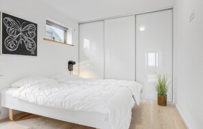 A modern bedroom with a large bed, a sliding door closet, a wall-mounted lamp, and a potted plant. - Lovely home in Rømø with sauna (Rømø)