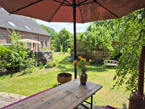 Une table en bois avec un vase de fleurs, placée sous un grand parasol dans un jardin.