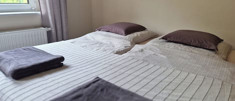 Ein Hotelzimmer mit Bett, Kissen, einem Fenster mit Vorhängen, einer Heizung und einem Bild an der Wand.