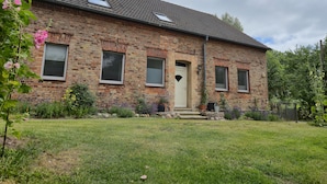 A two-story brick house with a tiled roof, a front door, and a small front yard with grass and plants. - Vacation apartment 2 - Green idyll (Borrentin)