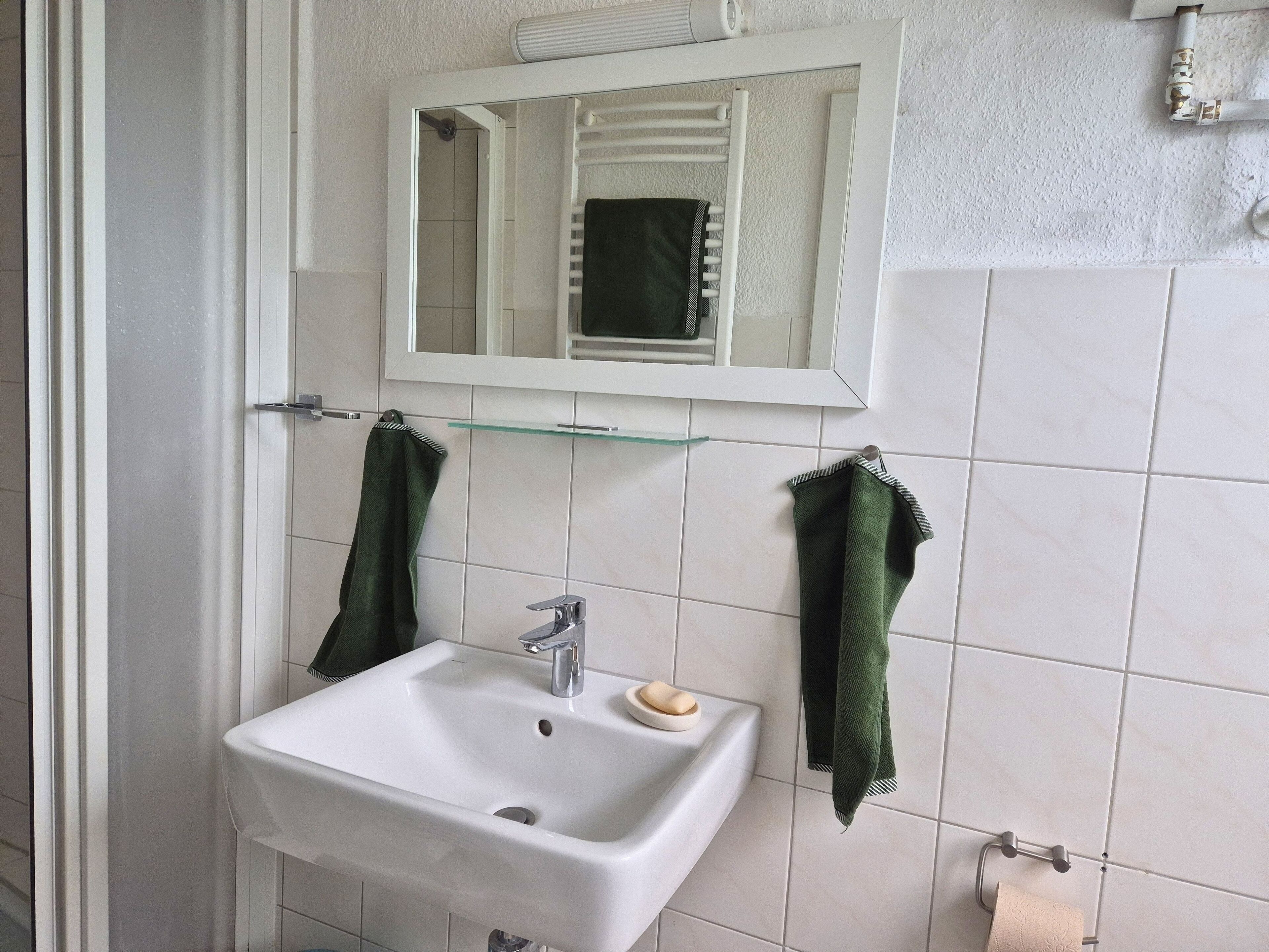 Un bagno con un lavandino bianco, uno specchio e due asciugamani verdi appesi a ganci.