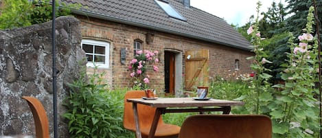A rustic outdoor seating area with a brick building, a wooden table, and chairs.