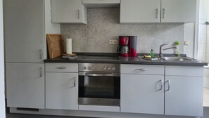 A modern kitchen with white cabinets, a stainless steel oven, a coffee maker, and a sink. - Vacation apartment 2 - Green idyll (Borrentin)