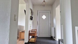 A hallway with a door, a radiator, a chair, and a hanging light fixture. - Vacation apartment 2 - Green idyll (Borrentin)