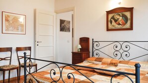 Een slaapkamer met een bed, twee stoelen, een deur en twee foto's in lijsten aan de muur.