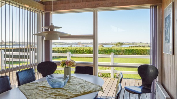 A dining area with a table set for two, a vase with flowers, and a view of a lake and greenery. - Awesome home in Hejls with sauna (Hejls)