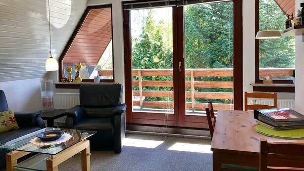 Ein gemütliches Zimmer mit einem Holztisch, einem Glastisch, einem schwarzen Ledersessel und einer Holzbank.