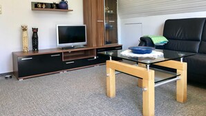 Ein modernes Wohnzimmer mit Flachbildfernseher, einer Holz-Unterhaltungseinheit, einem Glastisch und einem schwarzen Ledersofa.