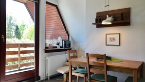 Ein Zimmer mit einem Holztisch, Stühlen, einem Heizkörper, einem Fenster mit Jalousien und einem Regal mit Dekoration.