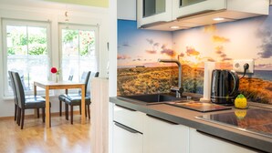 Een moderne keuken met een groot raam, een eethoek met een tafel en stoelen, en een muurschildering van een zonsondergang.