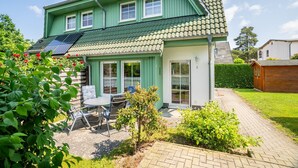 Een tweelaags huis met een groene gevel, een pannendak en een klein terras met een tafel en stoelen.