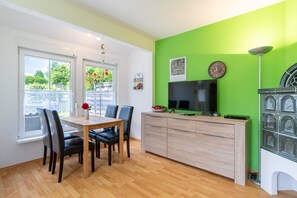 A modern kitchen with a dining area, featuring a wooden table, chairs, a TV, and a green accent wall.