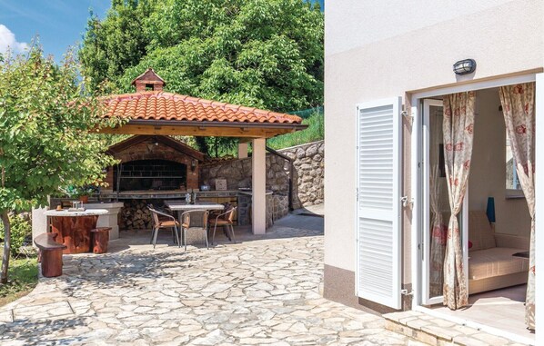 Una terrazza esterna con pavimento in pietra, un barbecue in mattoni e un tavolo con sedie.