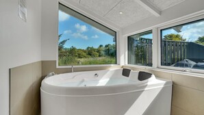 Une salle de bain moderne avec une baignoire sur pieds, de grandes fenêtres offrant une vue sur l’extérieur et un plafond orné d’un motif texturé.