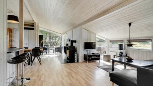 Un espacio habitable amplio con techo de madera, televisor, parrilla y disposición de asientos.