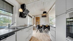 Una cocina moderna con armarios blancos, suelo de madera y sillas negras alrededor de una isla central.