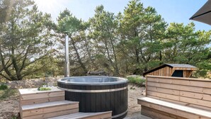 Un jacuzzi con escalones de madera, rodeado de árboles y una terraza de madera.