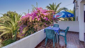 Ein Balkon mit Tisch und Stühlen, einem blauen Sonnenschirm und rosa Bougainvillea-Blumen.