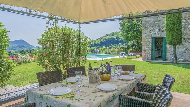 Ein Essbereich im Freien mit Tisch für vier Personen mit Blick auf einen Pool und einen üppigen Garten.
