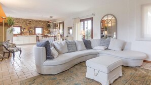 Ein geräumiges Wohnzimmer mit einer großen, L-förmigen Couch, einem kleinen weißen Hocker und einem gemusterten Teppich.