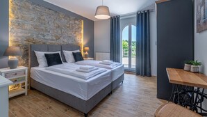 A modern bedroom with a stone accent wall, a large bed, bedside lamps, a view to the outdoors, and a small table with plants.