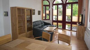 A room with a wooden floor, a black leather sofa, a wooden table, and a bookshelf.