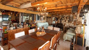 A rustic cabin interior with a wooden dining table, stone walls, and a stone fireplace.