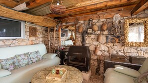 A cozy living room with a stone wall, a sofa, a round coffee table with a tray, a fireplace, and a television.