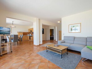 A living room with a sofa, a coffee table, and a TV. There is a kitchen in the background with cabinets and a dining area. - MB. 4 17 - Ocean View Apt. MB-417 .. (Kühlungsborn)