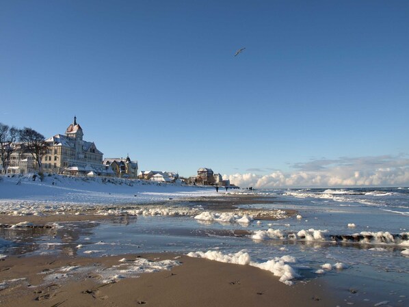 Un pueblo costero con edificios históricos, una playa cubierta de nieve y hielo, y un cielo despejado.