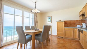Zona pranzo con vista sul mare, un tavolo in legno, quattro sedie e una lampada a sospensione.