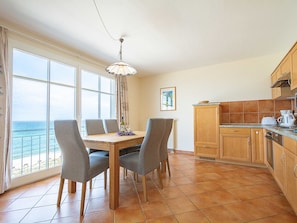 A dining area with a view of the sea, a wooden table, four chairs, and a hanging light fixture.