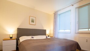 Una camera da letto con un letto, comodini, un quadro appeso al muro e una finestra con persiane.