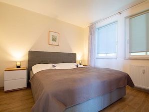A bedroom with a bed, bedside tables, a framed picture on the wall, and a window with blinds.