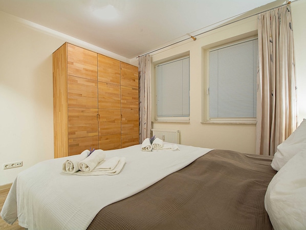 A bedroom with a bed, a wooden wardrobe, and a window with blinds.