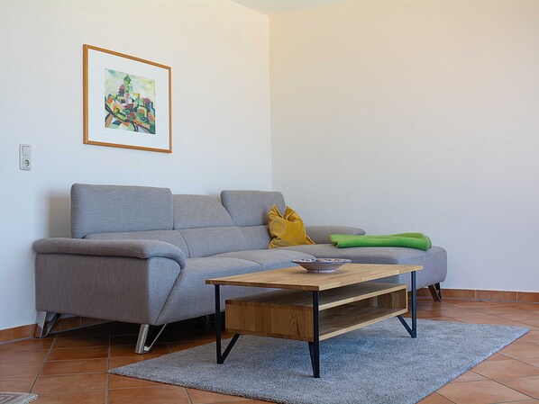 A living room with a grey sofa, a wooden coffee table, a green throw blanket, and a framed abstract painting on the wall. - MB. 4 17 - Ocean View Apt. MB-417 .. (Kühlungsborn)