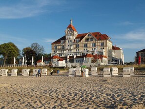 A large building with multiple balconies and a red roof, situated on a sandy beach.