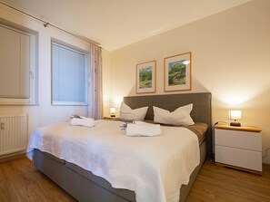 A neatly made bed with white linens, two bedside lamps, and two framed pictures on the wall.