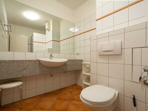 Un baño con lavamanos, espejo, inodoro y secamanos.
