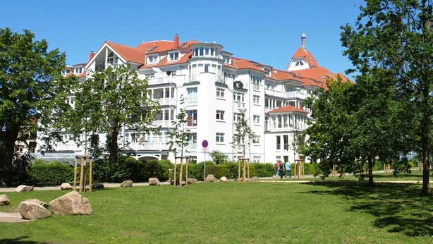 Un grande edificio bianco con tetti rossi, numerosi balconi e un parco sullo sfondo.