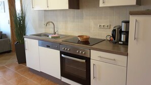 Cozinha moderna com armários brancos, exaustor de aço inoxidável, lava-louças, forno e cafeteira na bancada.